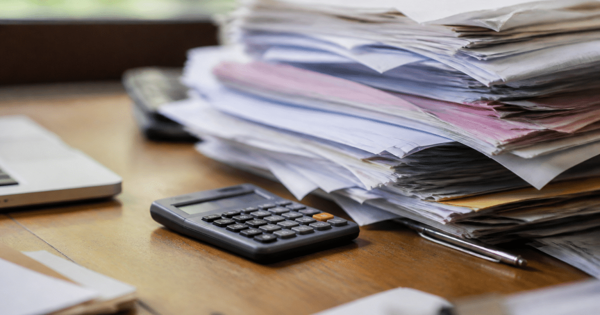 Factures et documents empiles sur bureau avec calculatrice